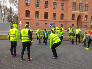 przed budynkiem urzędu miejskiego w Mrągowie biegacze ubrani w kamizelki odblaskowe