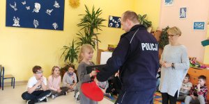 szkolna klasa, policjant wręcza nagrody dziewczynce na podłodze siedzą dzieci