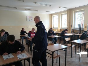 test wiedzy w klasie, w ławkach siedzą uczniowie policjant rozdaje testy