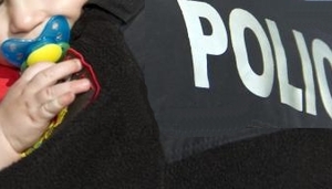 ręka dziecka i smoczek w buzi i koszulka z napisem policja