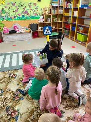 w szkolnej sali policjantka siedzi na dywanie i czyta siedzącym wokół niej dzieciom bajkę