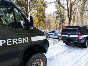 w lesie zimą stoją w lesie radiowóz policyjny i dwa pojazdy patrolu saperskiego