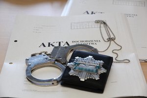 akta dochodzenia na których leżą kajdanki i odznaka policyjna