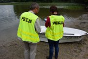 dwie osoby w kamizelkach odblaskowych stoją przy łódce, która stoi na brzegu