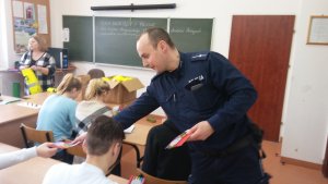 szkolna klasa, policjant przekazuje uczniom ulotki